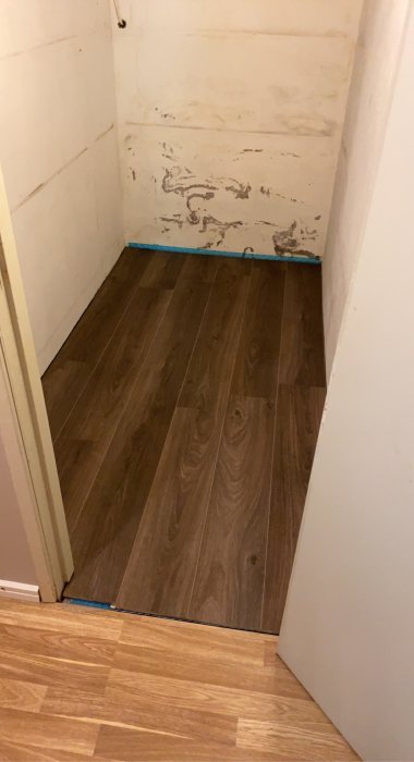 Nyinstallerat mörkt trägolv i en tom matkällare med vita väggar och tecken på renovering.