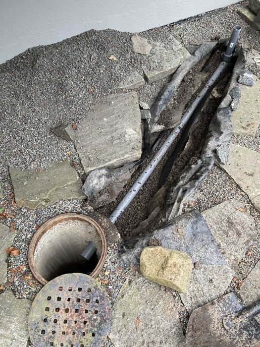 Nyinstallerat 50-rör vid brunnen, omgivet av grus och duk, med påbörjad återfyllning och uppbrutna stenplattor runtomkring.