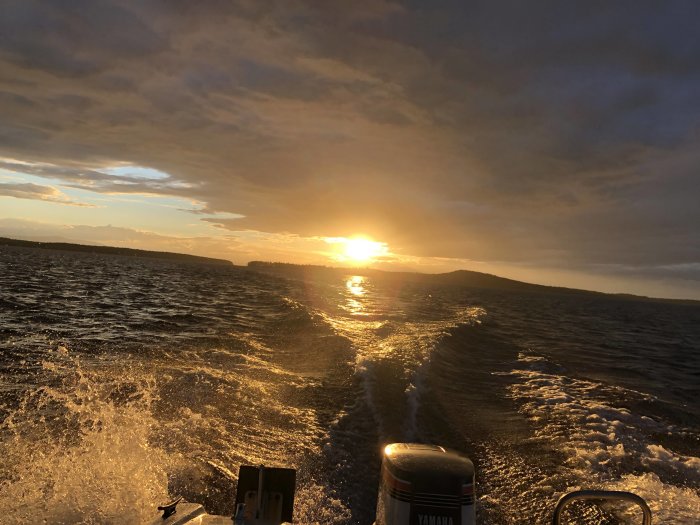 Solnedgång över havet sedd från en båt med skummande vågor och motorn i förgrunden.