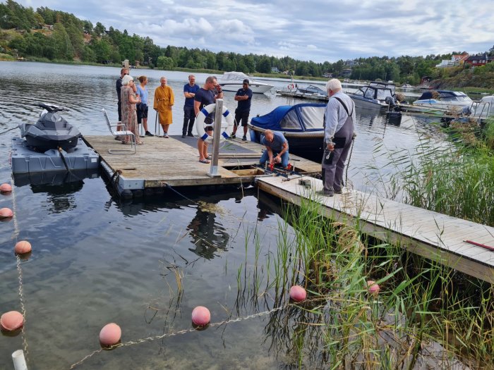 Personer står på en nyförstärkt brygga vid en sjö medan en person arbetar på konstruktionen.