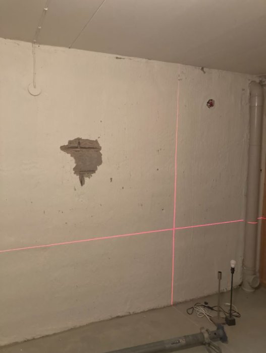 En vit vägg med ett litet hål och röda laserlinjer som markerar mätningar för renovering.