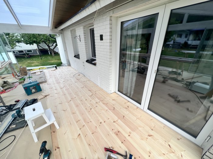 Nylagt ljust trägolv på veranda med verktyg och byggmaterial, vita väggar och skjutdörrar.