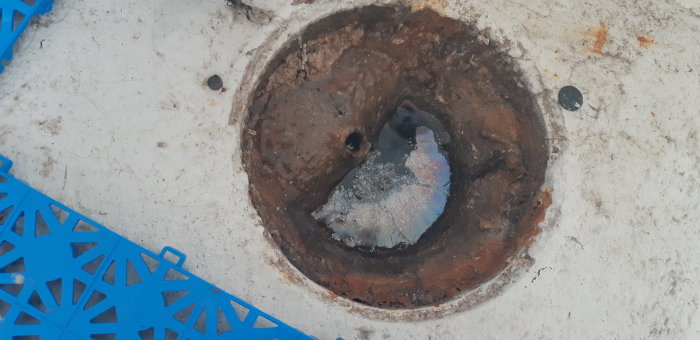 Rostig avloppshålighet i betong med blå plastskydd nära kanten.