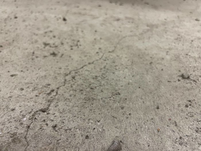 Närbild på en sprucken betongyta med synliga småstenar och dammpartiklar.