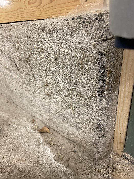 Närbild av en betongvägg med tecken på slitage och nedbrytning vid kanten nära träram.