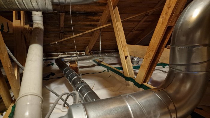Ventilationsrör som är upphängda i ett öppet bjälklag under en takkonstruktion i ett pågående byggprojekt.