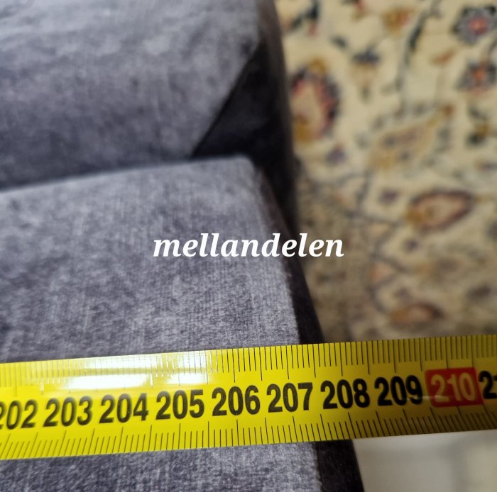 Måttband visar en längd på en soffas mellandel, texten "mellandelen" framför tyget.