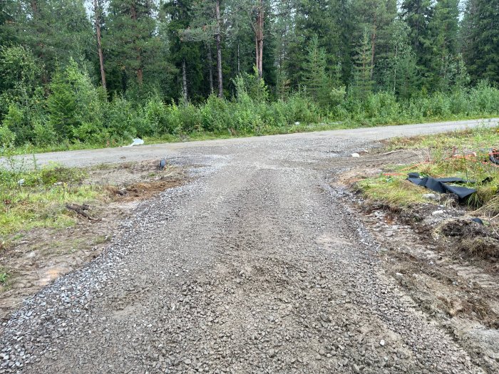 Grusad infartsväg under anläggning med grävmaterial vid sidan, omgiven av skog.