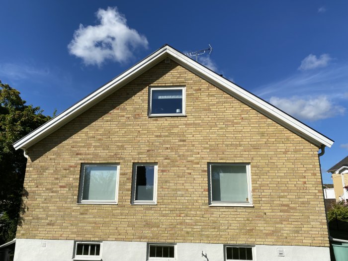 Gavelvy av ett tegelhus med tre fönster under en klarblå himmel.