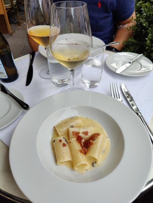 En tallrik med pasta i krämig sås serveras på en restaurang, med vinglas och vatten i bakgrunden.