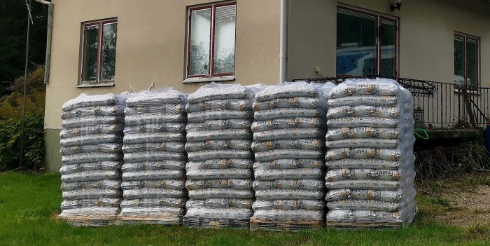 Staplar med pellets i plastförpackning framför ett hus, likt en värdetransport.