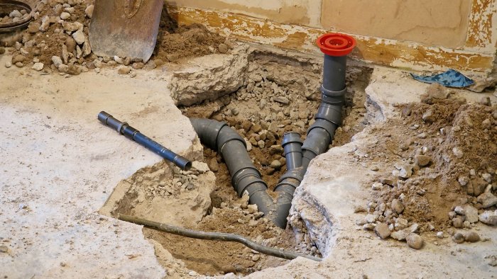 Nytt avloppssystem och golvbrunn under installation i betonggolv med rör och grus.