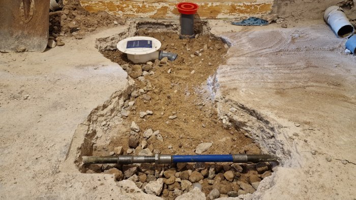 Renoverat golv med ny golvbrunn, avloppsrör för vask/tvättmaskin och framgrävda grus och betongytor.
