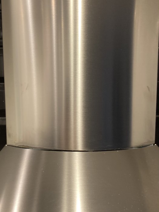 Närbild på en rostfri köksfläkt ovanför en spishäll med synliga borstad yta och skarvar.