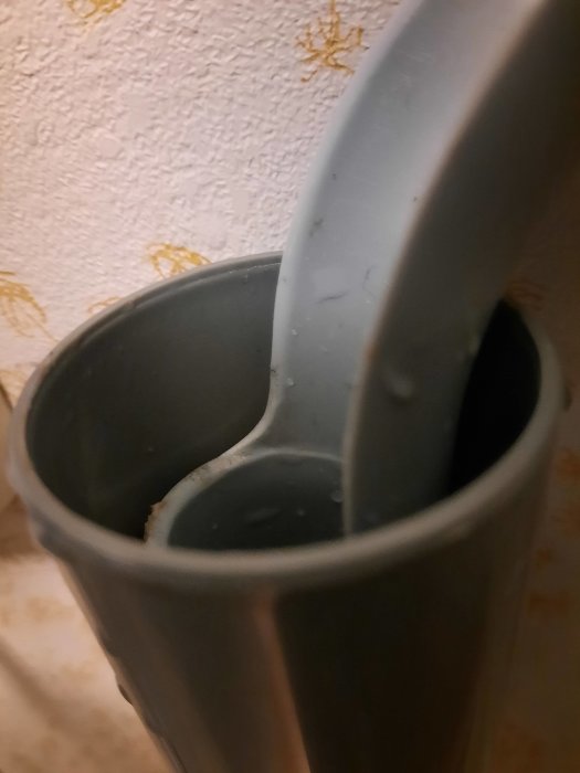 Grå plastslang från tvättmaskin ansluten till grått avloppsrör mot tapetserad vägg.