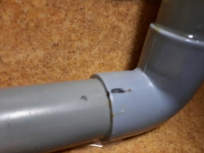 Närbild på grått avloppsrör med en böj nära golvet, möjligtvis gammalt, med tecken på slitage.