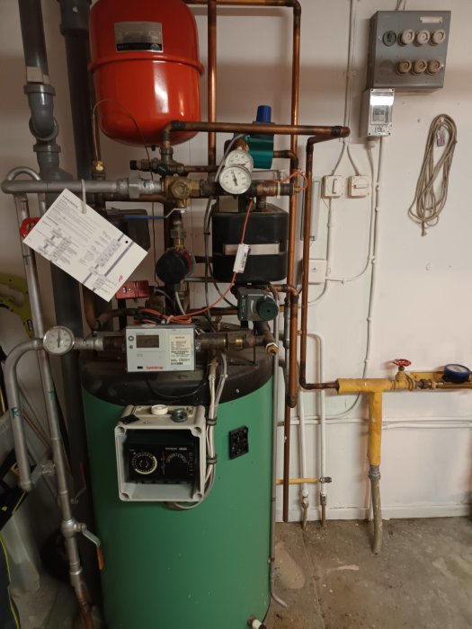 Värmepannrum med grön vattentank, kopparledningar, expansionskärl och mätare.