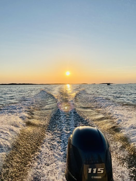 Solnedgång över havet sett från en båt med motor och krusningar i vattnet.
