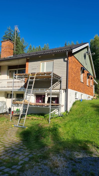 Ställning utanför ett tvåvåningshus med tegelvägg under renovering mot en klarblå himmel.