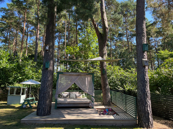 Trädgård med hemmasnickrad cabana på trädäck omgiven av träd och leksaker.