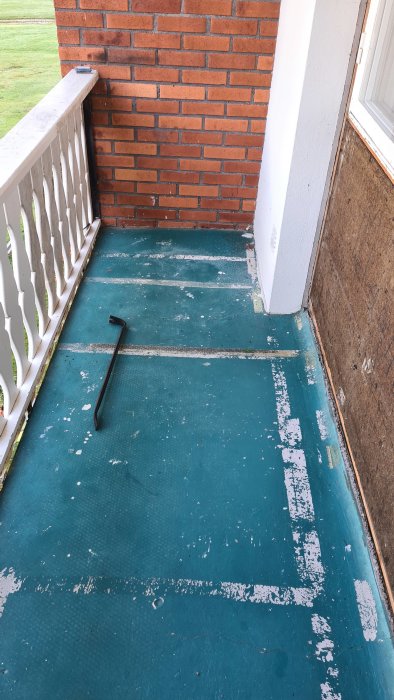 Balkonggolv med slitna gröna ytskikt och ett svart verktyg på golvet.