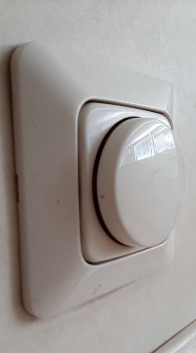 Vit termostatreglage på en vägg, lite smutsig och sliten, indikerar en fråga om termostatjustering.