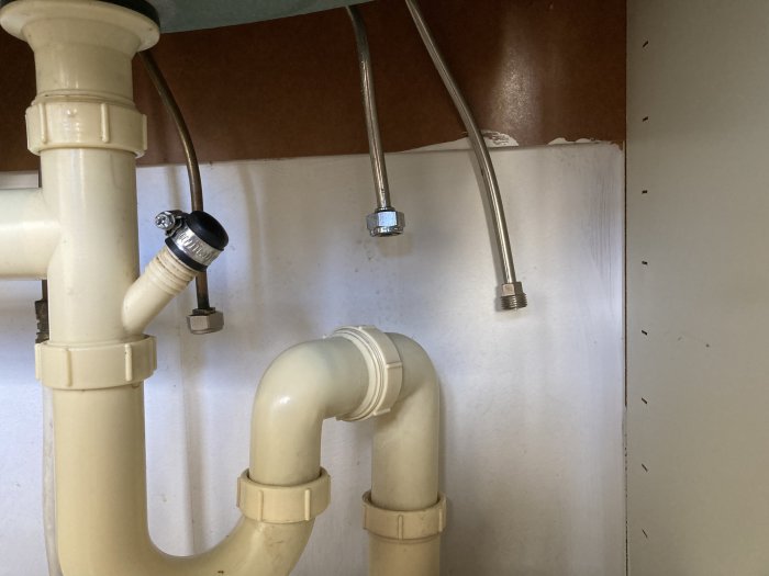 Vattenrör och avloppsrör under diskbänk med kopplingar för kökskran.