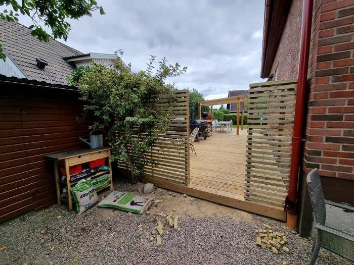 Nyligen färdigställd trall med dubbel fris och ribbstaket vid ett hus, ofärdig grundmur och material syns.