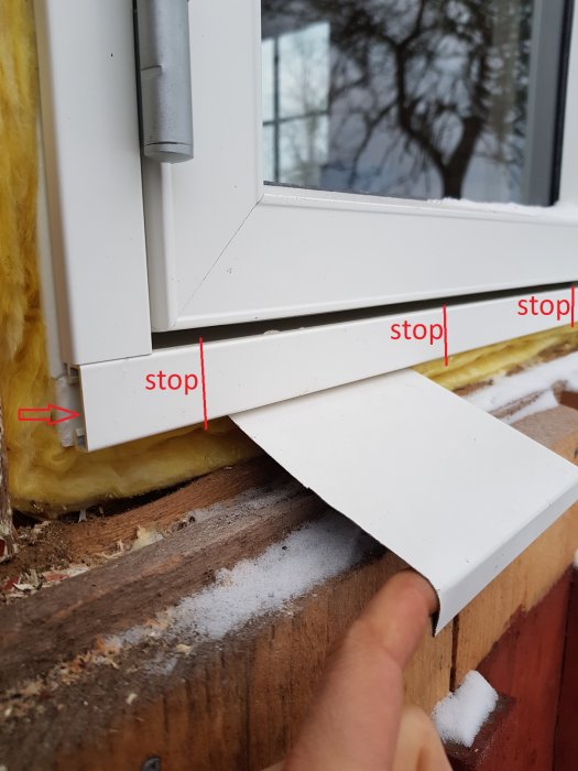 Hand som håller ett vitt metallbleck nära aluramens fästen på en husvägg med texten "stop" markerad på flera ställen.