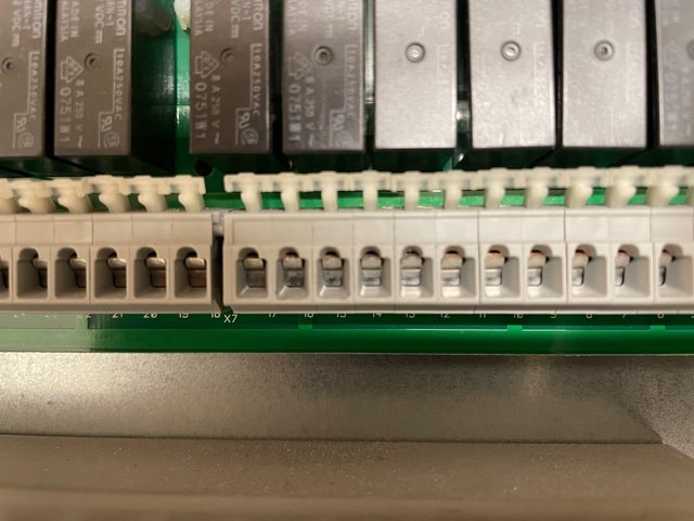 Elektrisk kopplingsplint med märkta anslutningar och reläer i bakgrunden.