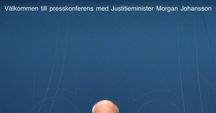 Presskonferensbakgrund med texten "Välkommen till presskonferens med Justitieminister Morgan Johansson" och en persons huvud synligt.