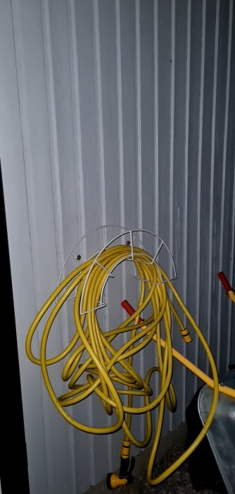 Slangvinda med gul kabel upphängd på vägg i rörigt tillstånd.