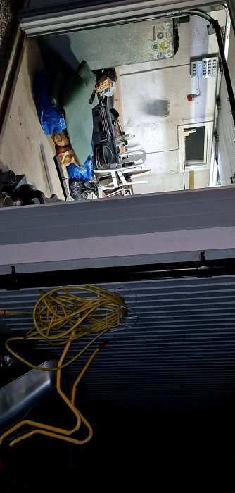 Vy från en öppen garageport ner till en rörigt organiserad källare med diverse föremål.
