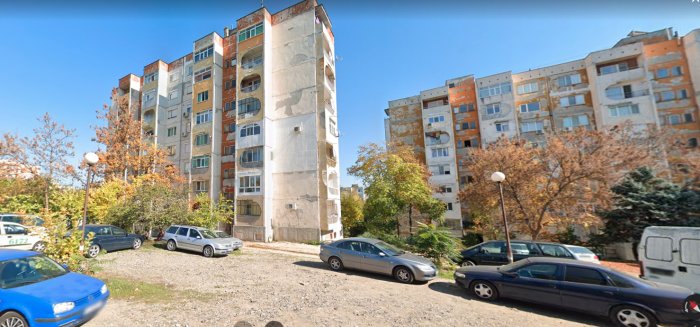 Bild på ett bostadshus med olikformade balkonger och parkerade bilar på en grusplan.