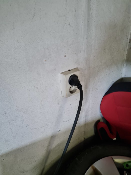 Enkelt eluttag i garage med insatt sladd och delvis synligt bildäck.