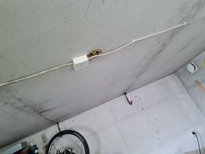 Enkelt eluttag på en betongvägg i ett garage med synliga kablar löpande längs väggen och taket.