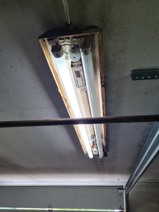 Undersida av öppen lysrörsarmatur med eluttag i ett garage.