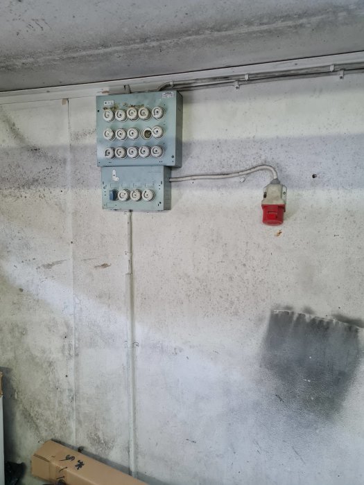 Elskåp med flera tomma uttag och ett ensamt rött vägguttag i ett garage.
