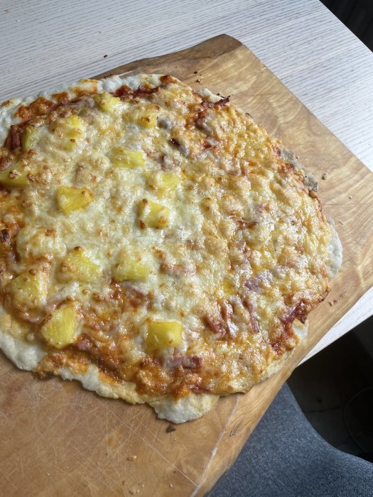 Hemgjord pizza med ananas och riven ost på ett träskärbräde.