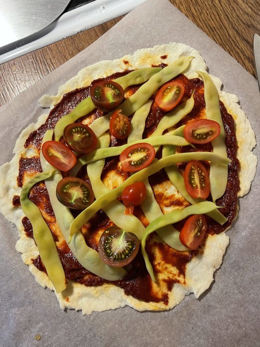 Hemgjord pizza med tomatsås, vaxbönor, halverade körsbärstomater på ett ugnsbakat pizzabottn.