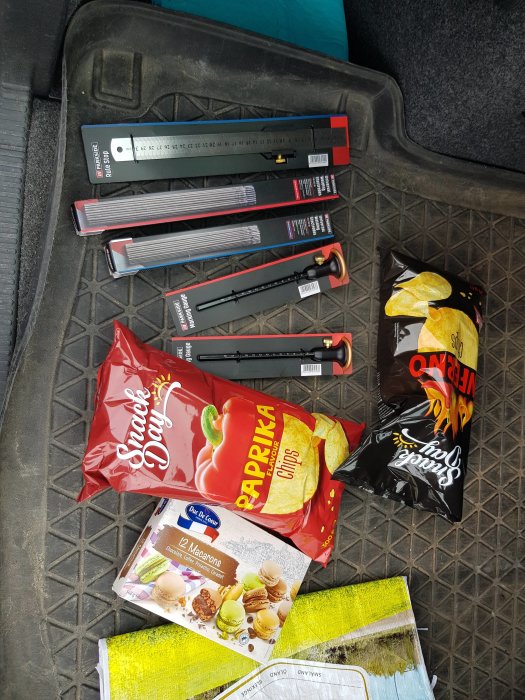 Byggmaterial och snacks i ett bilbagage, inklusive vattenpass, chips och macarons, men ingen mjölk.