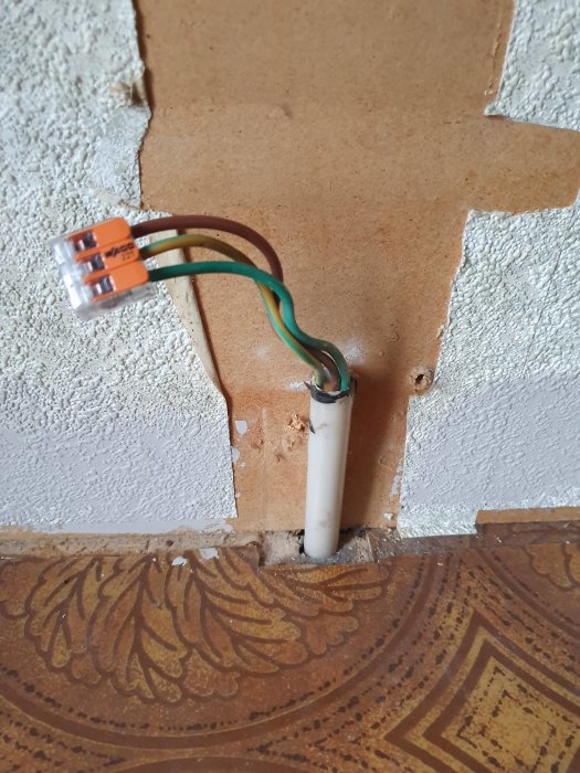 Elektriska kablar kopplade med en WAGO-klemme som sticker ut ur en vägg ovanför en brun kakelplatta.