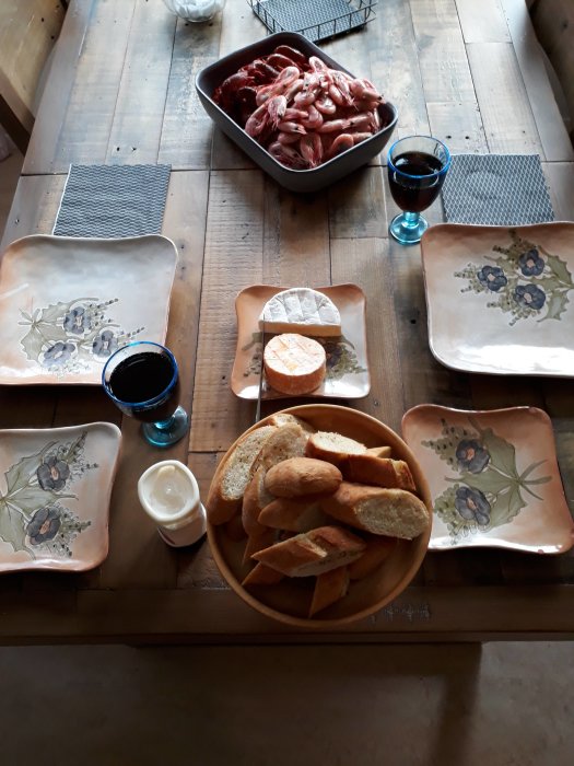 Kräftor och räkor i en skål, ost och baguette på träbord med vin och dukar.