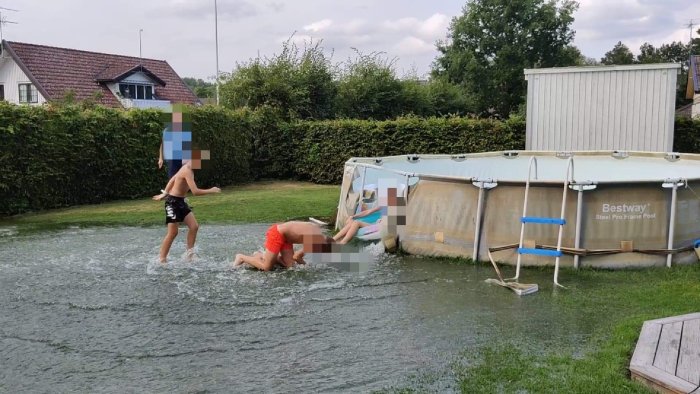 Två personer leker i vattensamling bredvid en kollapsad ovanmarkspool.