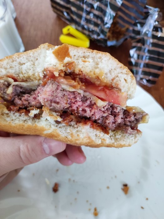 Halväten hamburgare hållen i en hand med synligt kött, ost och tomat.