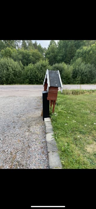 Ny stor brevlåda monterad på en stötta vid en grusgång, omgiven av grönt gräs och träd i bakgrunden.