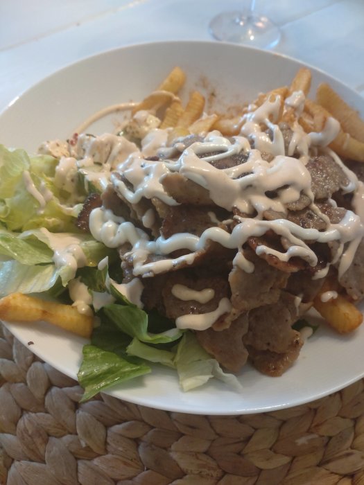 Tallrik med kebabkött, pommes frites och sallad toppad med vit sås.