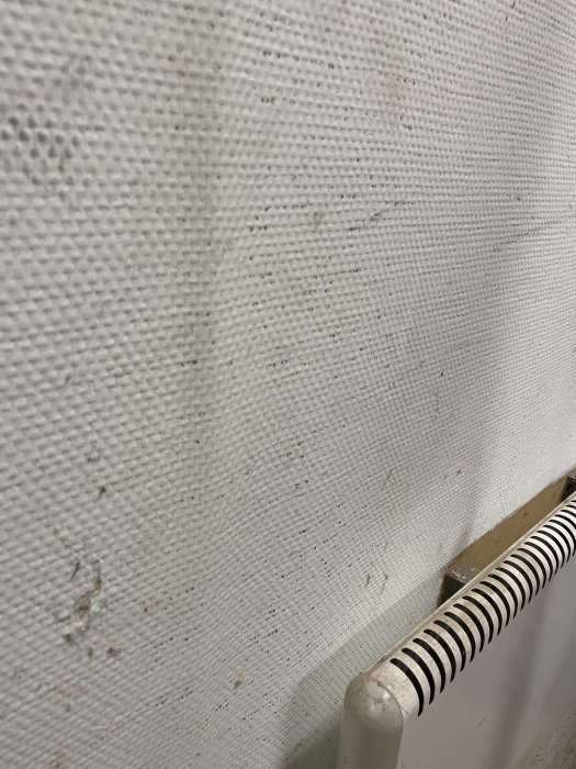 Närbild på en vit texturerad vägg med mindre smutsfläckar och en radiator i förgrunden.