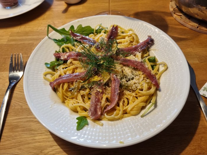 Tallrik med pasta toppad med parmesan, karamelliserad fänkål och sardeller på ett träbord.