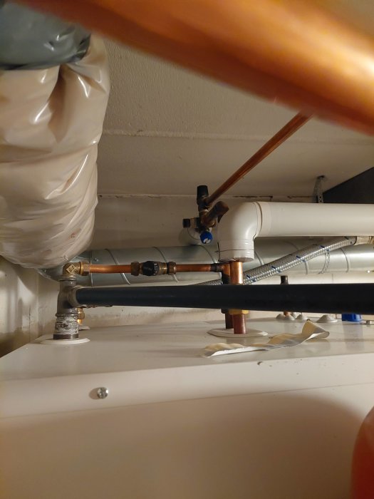 Rörinstallation under diskbänk med koppar- och plastledningar samt avstängningsventiler.